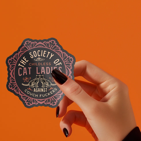 Round sticker with ornate border showing two cats and text "The Society of Childless Cat Ladies Against Couch Fuckers" in pink and purple versions on black background.